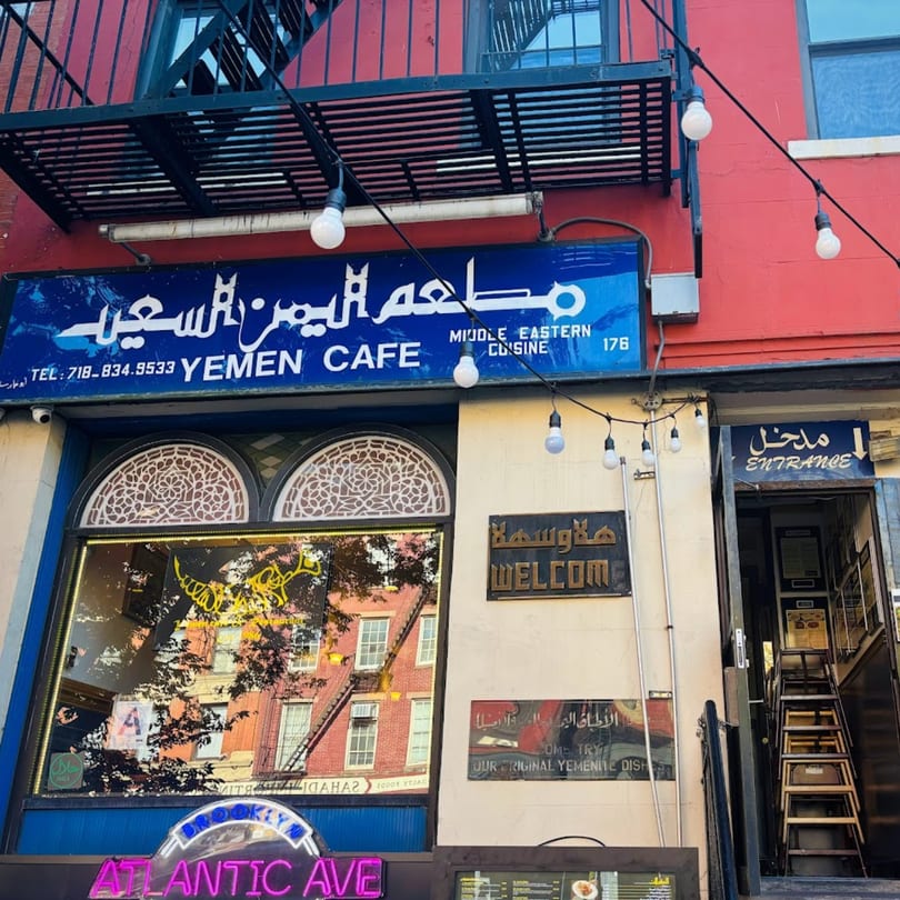 The vibrant blue and red exterior of Yemen Cafe, a Middle Eastern restaurant, with string lights and a welcome sign.