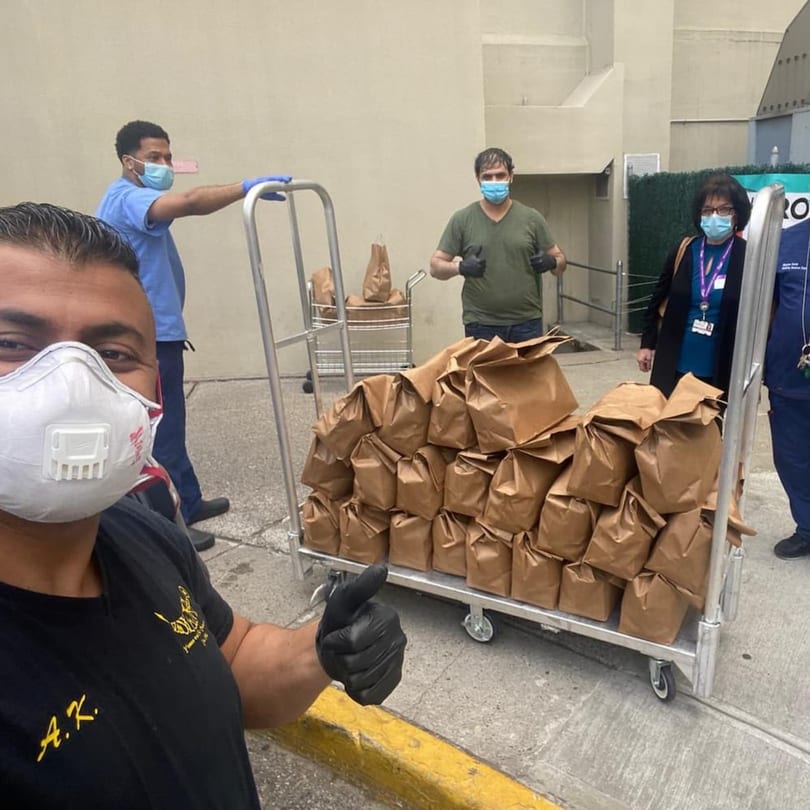 Four masked people with two carts full of brown paper bags of food from Yemen Cafe & Restaurant.
