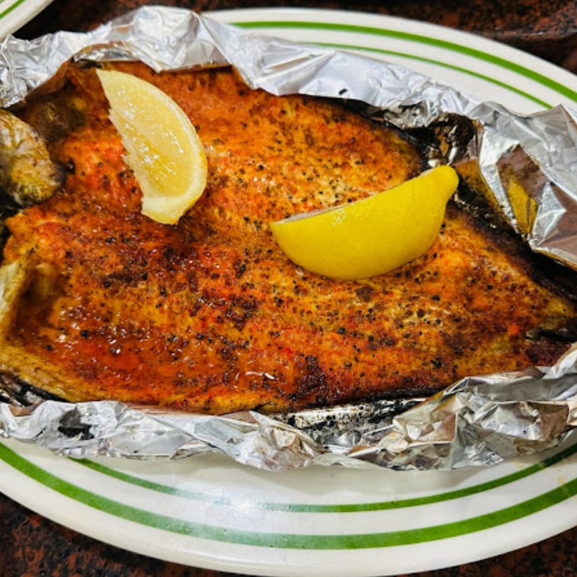 Baked fish with spices and two lemon wedges, served in foil on a white plate with green stripes.