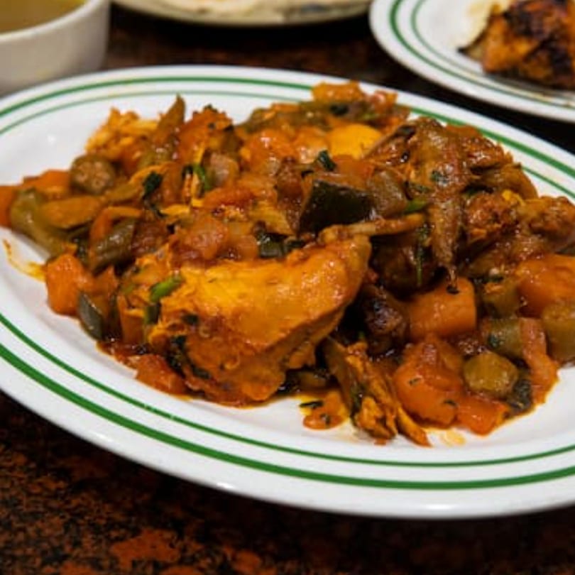 A close-up of a white plate with green stripes, filled with a hearty Middle Eastern stew.