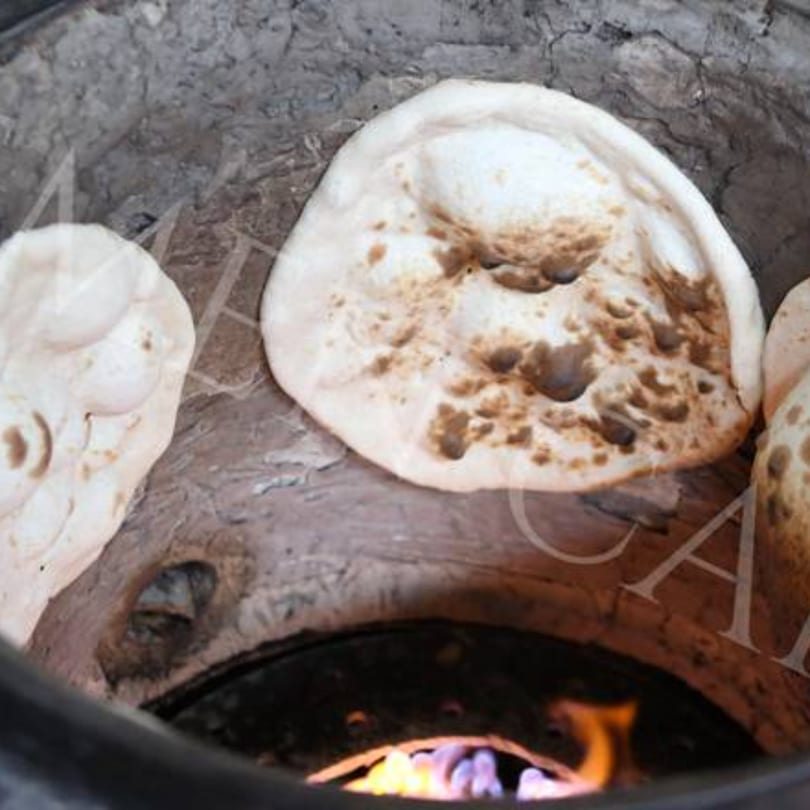 Freshly baked flatbreads cooking on the side of a traditional tandoor oven with flames visible below.