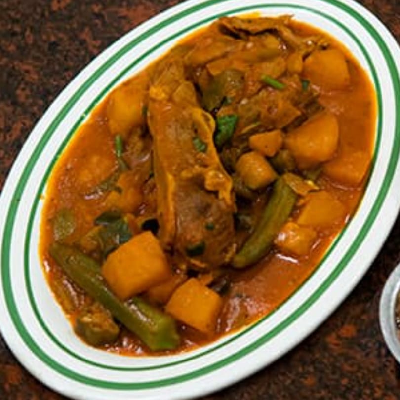 Yemeni lamb stew with potatoes and okra in a rich red sauce, served on a white plate with green stripes.