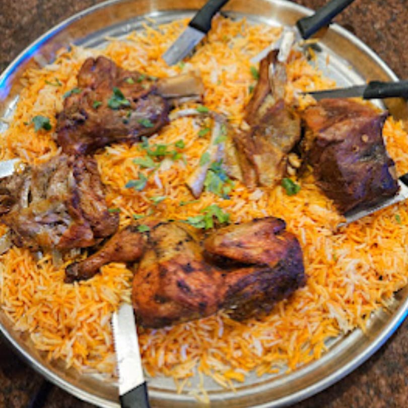 Large platter of Middle Eastern mandi rice with roasted chicken and lamb, garnished with cilantro.
