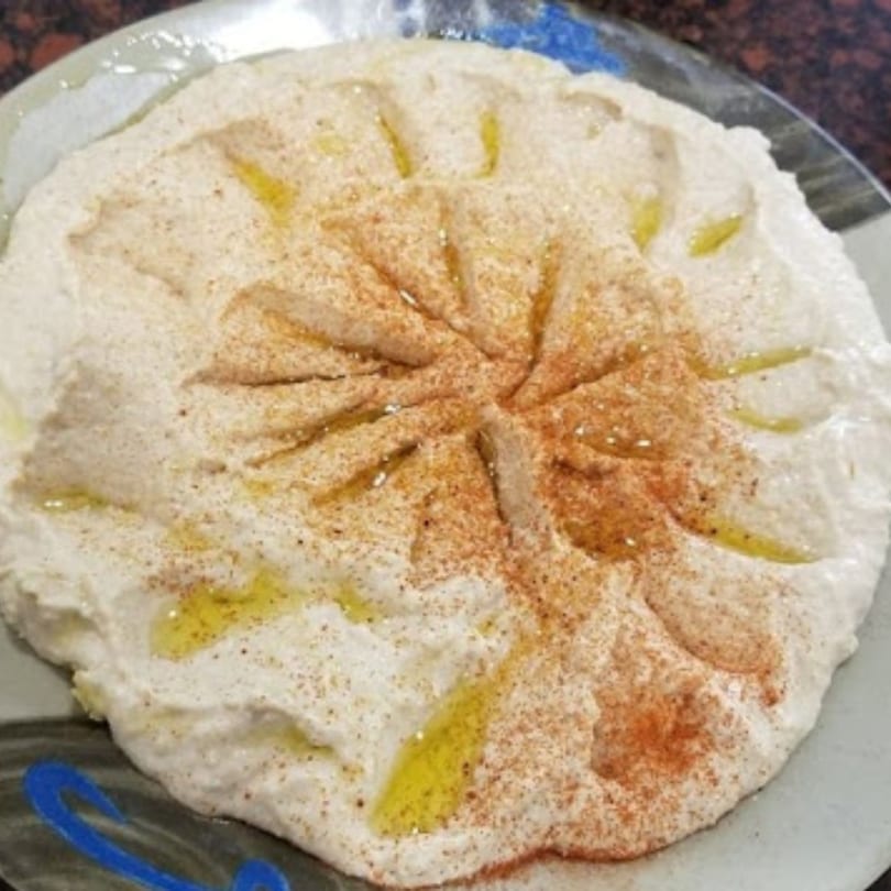 A plate of creamy hummus, drizzled with olive oil and sprinkled with paprika.