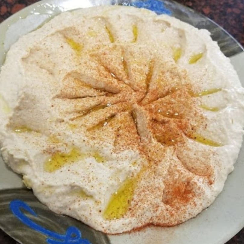 Creamy hummus drizzled with olive oil and sprinkled with paprika on a decorative plate.