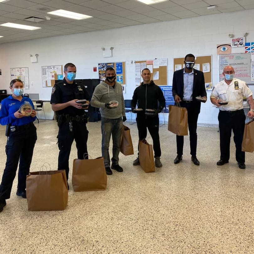 Six people, including police officers, hold Yemen Cafe food containers and brown bags in a room.