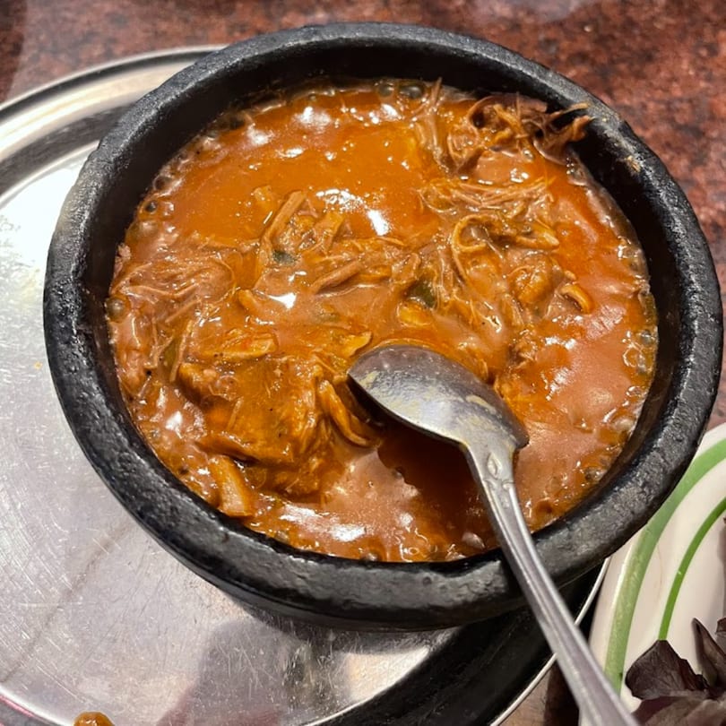 A black bowl filled with a rich, orange-brown stew, with a spoon resting inside.