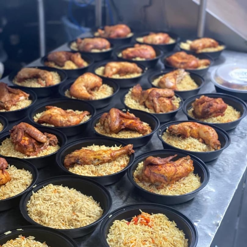 Rows of Yemen Cafe's roasted chicken and rice meals in black takeout containers on a metal counter.