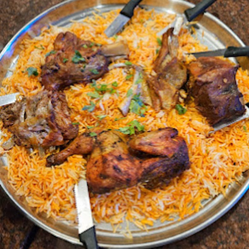 A large platter of Yemeni mandi rice with roasted chicken and lamb, garnished with fresh herbs.
