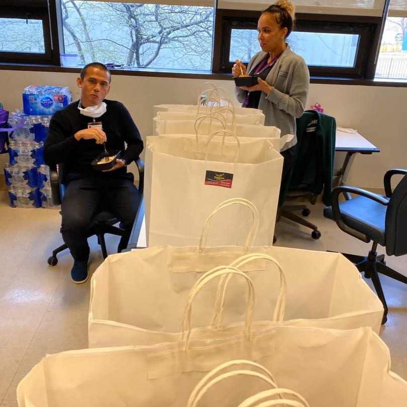 Two people eating from black bowls, surrounded by several large white takeout bags from Yemen Cafe.