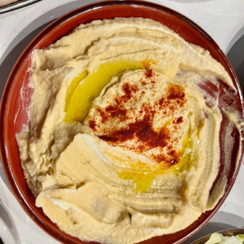 Creamy hummus in a rustic brown bowl, drizzled with olive oil and sprinkled with paprika.