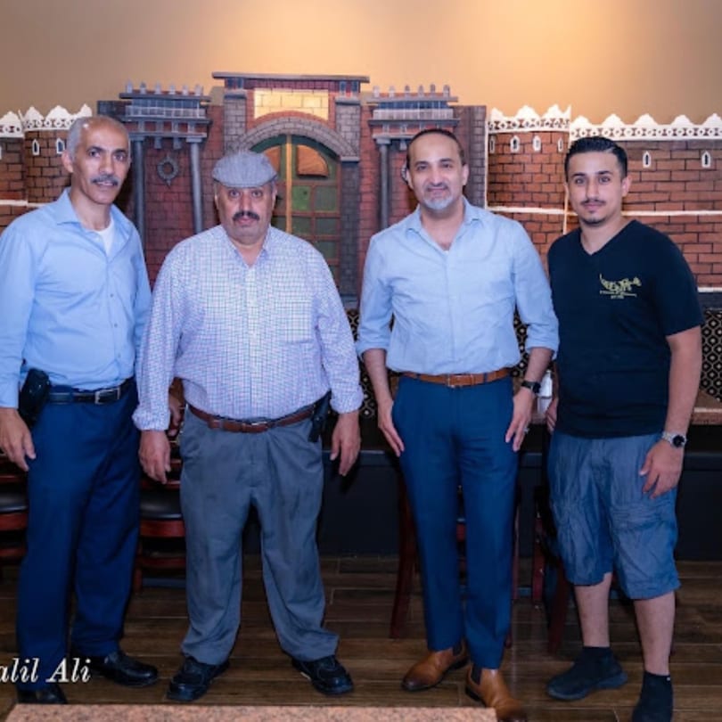 Four men standing in front of a decorative brick wall with archways and battlements at Yemen Cafe.