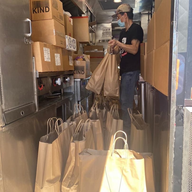 A person in a food truck fills numerous brown paper bags with orders from Yemen Cafe & Restaurant.