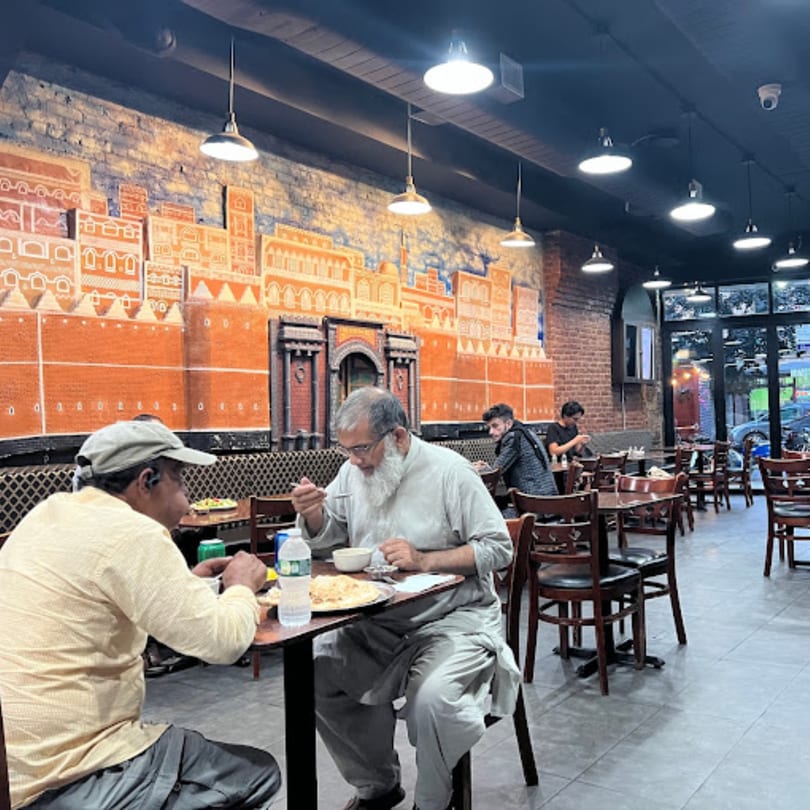 Diners eating at tables in Yemen Cafe & Restaurant, with a mural of a Middle Eastern city on the wall.