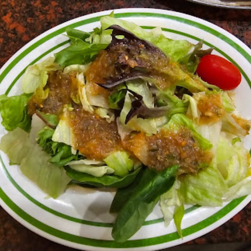 A fresh green salad with mixed greens, a single cherry tomato, and a savory dressing.