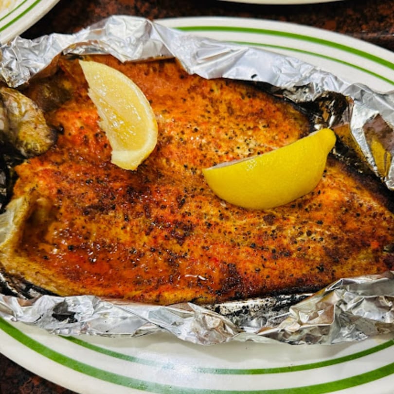 Whole baked fish, seasoned and served in foil with lemon wedges at Yemen Cafe & Restaurant.