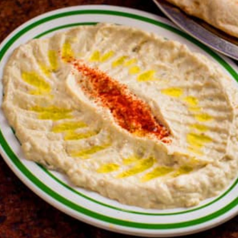 Creamy baba ghanoush topped with olive oil and red paprika on a white plate with green stripes.