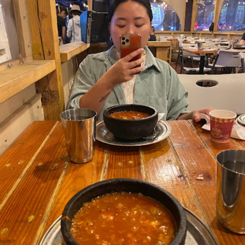 A person takes a photo of two bowls of Middle Eastern stew on a wooden table at Yemen Cafe.
