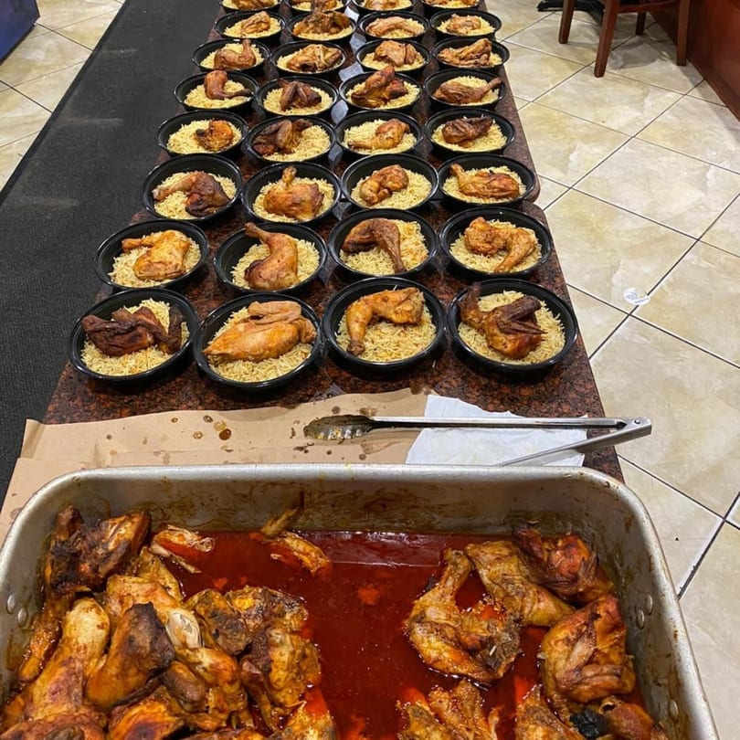 Rows of Yemen Cafe's Middle Eastern chicken and rice meals in black bowls, with a tray of roasted chicken.