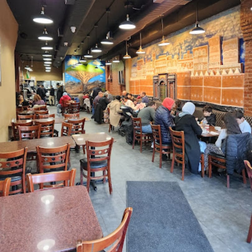 A bustling Middle Eastern restaurant interior with patrons dining at tables and decorative wall murals.