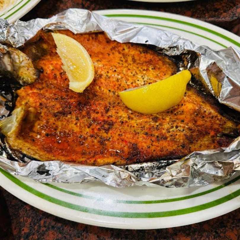 Whole baked fish with crispy skin and two lemon wedges, served in foil on a white plate.