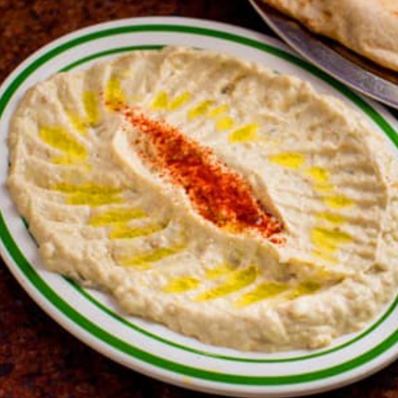 Creamy hummus or baba ghanoush with olive oil and red spice on a white plate with green stripes.