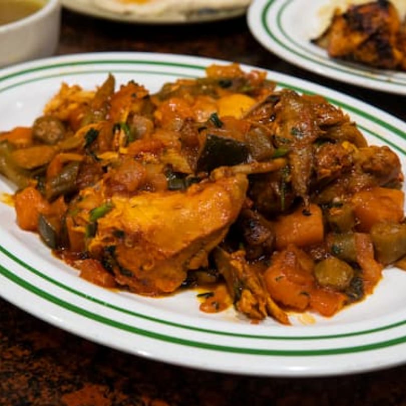 A close-up of a white oval plate with green stripes, filled with a hearty Middle Eastern stew.