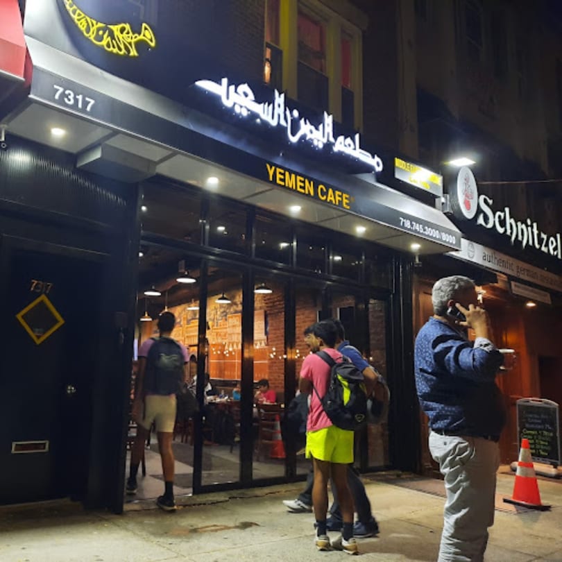 Exterior of Yemen Cafe & Restaurant at night, with glowing signs and people entering the establishment.
