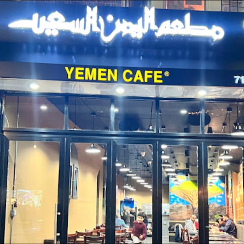 Exterior view of Yemen Cafe & Restaurant with its illuminated sign and patrons visible inside.