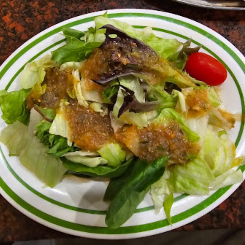 A fresh side salad with mixed greens, dressing, and a single cherry tomato on a white plate.