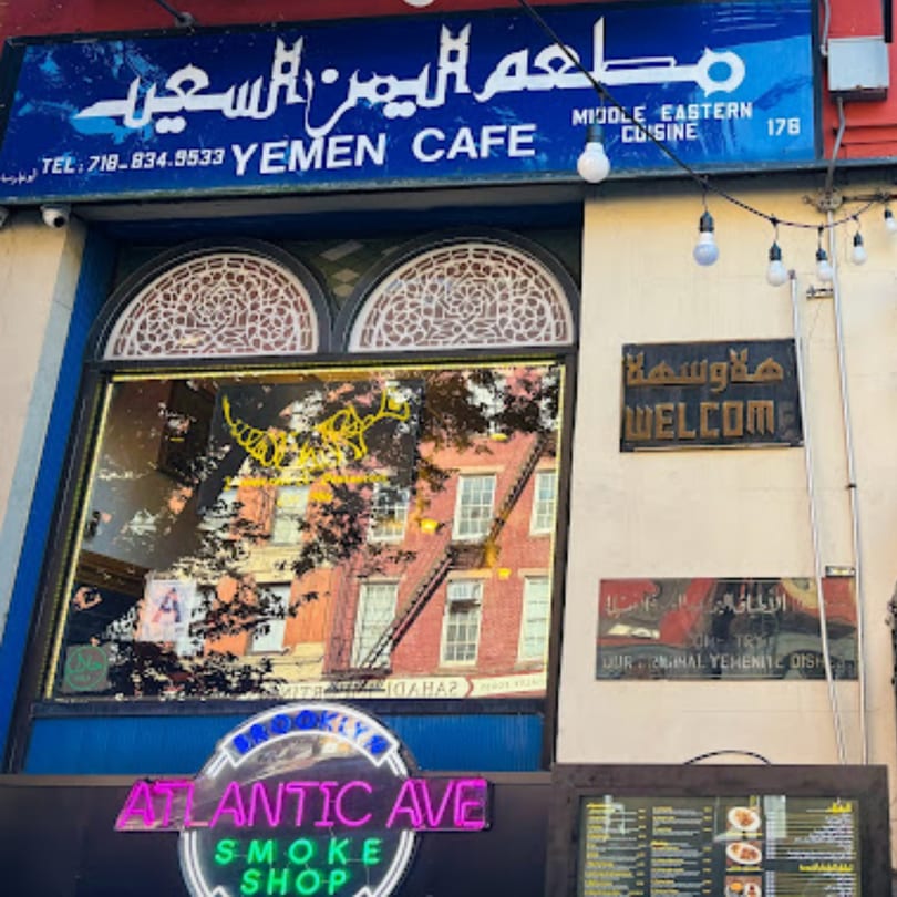 Exterior of Yemen Cafe & Restaurant with blue signage, ornate windows, and a 'Welcome' sign.