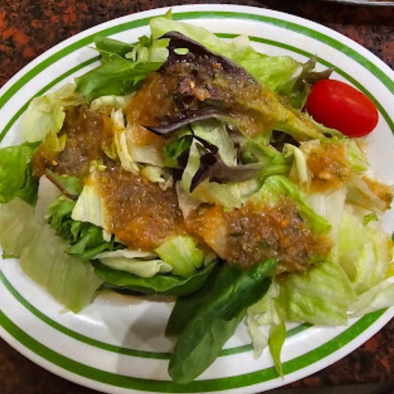 A fresh green salad with mixed greens, a single cherry tomato, and a savory dressing.