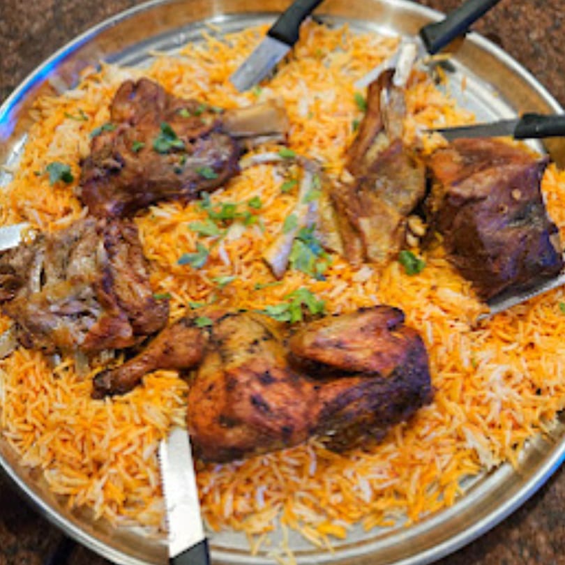 Large platter of Middle Eastern mandi rice with roasted chicken and lamb, garnished with parsley.