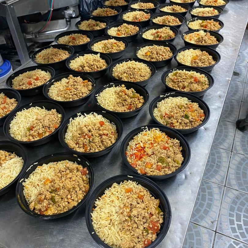 Rows of black bowls filled with Yemeni rice and seasoned ground meat on a metal counter.