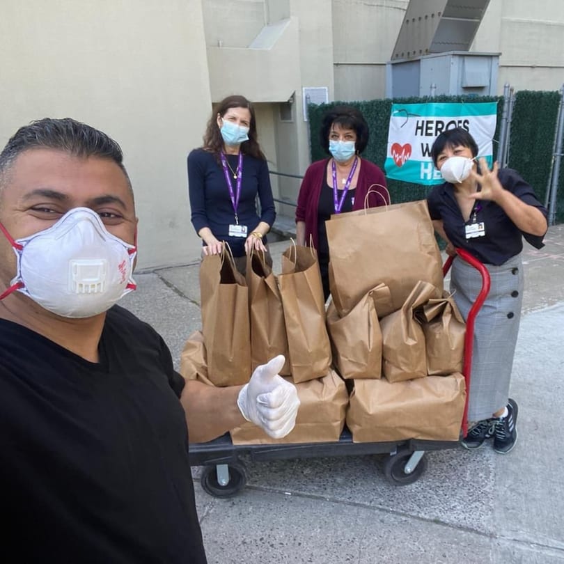 Four masked people, including a Yemen Cafe staff member, with a cart full of food bags for heroes.