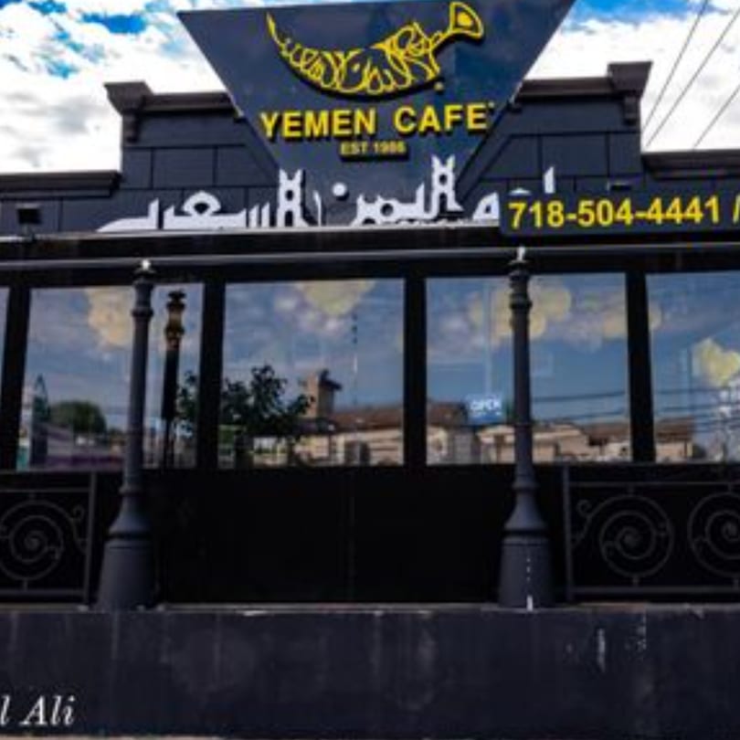 Exterior of Yemen Cafe & Restaurant, a black building with large windows and yellow signage.