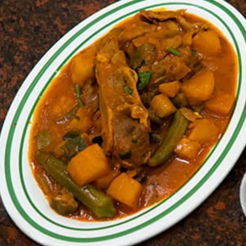 Hearty Yemeni stew with lamb, potatoes, and okra in a rich, orange sauce on a white plate.